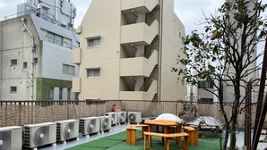A rooftop terrace with multiple air conditioning units, a wooden table and chairs, and a small tree. - Asakusa Ryokan Toukaisou (Tokyo)