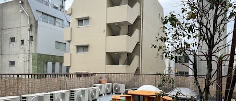 Una terraza en la azotea con varias unidades de aire acondicionado, una mesa y sillas de madera, y un pequeño árbol.