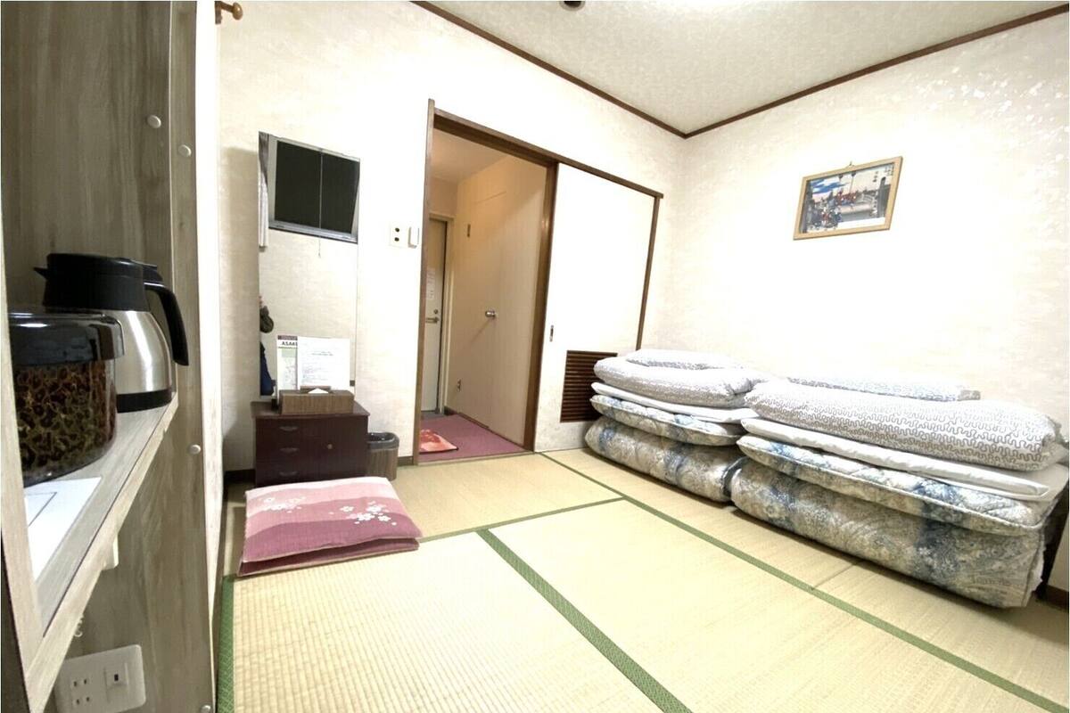 Een kamer met tatami matten, een bed, een verwarming, een televisie en een deur naar een andere kamer.