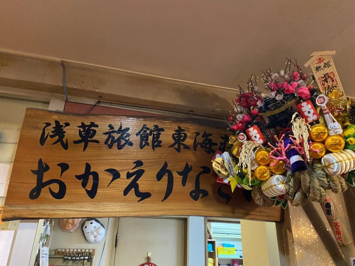 Un letrero de madera con caracteres japoneses, un colorido arreglo de flores y adornos, y un reloj en la pared.