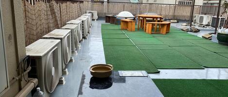 Una terraza en la azotea con unidades de aire acondicionado, una zona de césped artificial verde y mobiliario de madera.