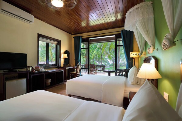 A hotel room with two beds, a TV, a desk, and a view of greenery outside. - Lang Co Beach Resort (Phu Loc)