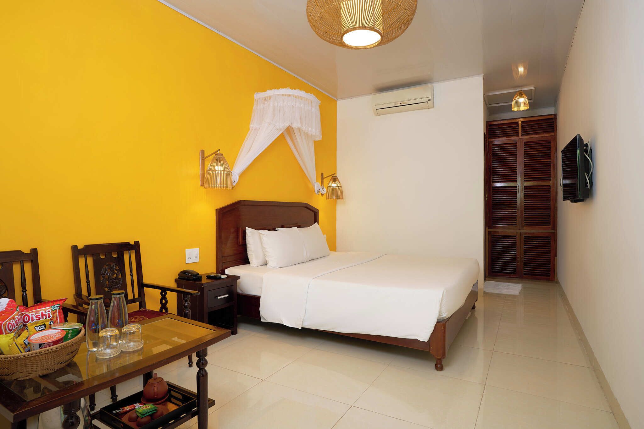 A bedroom with a bed, bedside table, and a chair. There is a window with wooden shutters, an air conditioning unit, and a ceiling light fixture.