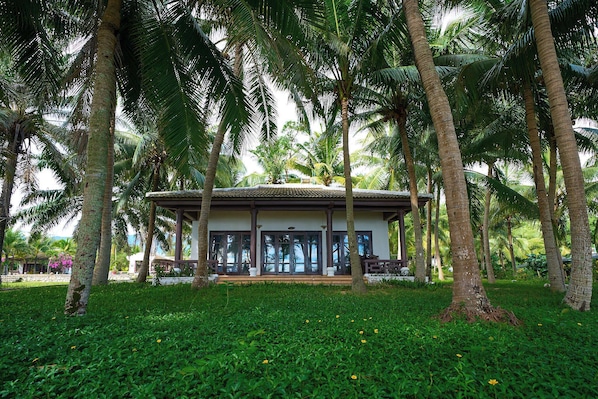 A building with a covered patio, surrounded by palm trees and lush greenery. - Lang Co Beach Resort (Phu Loc)