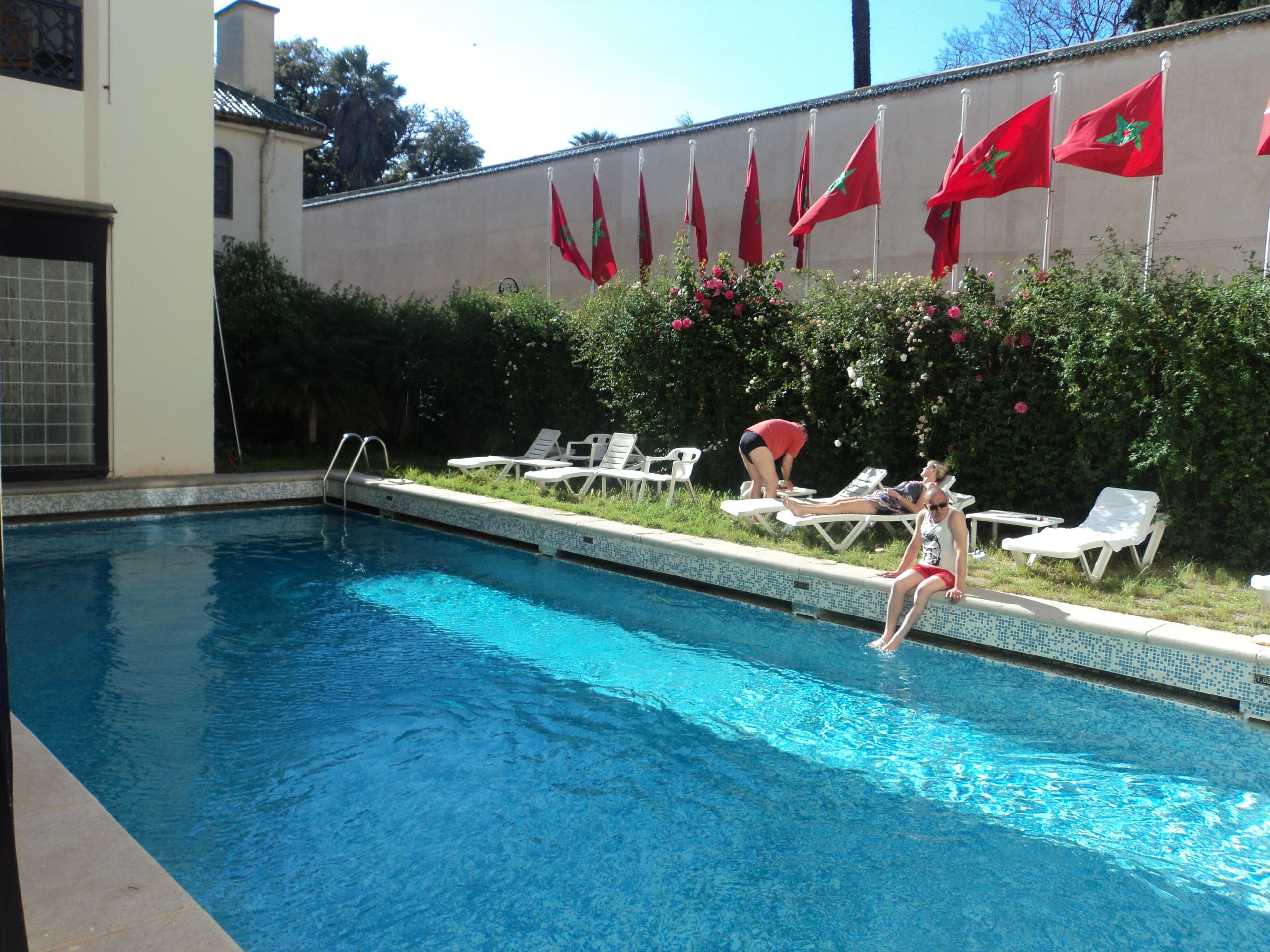A swimming pool with lounge chairs and flags on a wall.