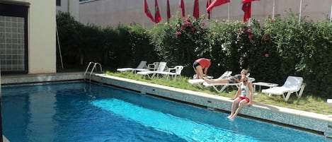 A swimming pool with lounge chairs and flags on a wall.