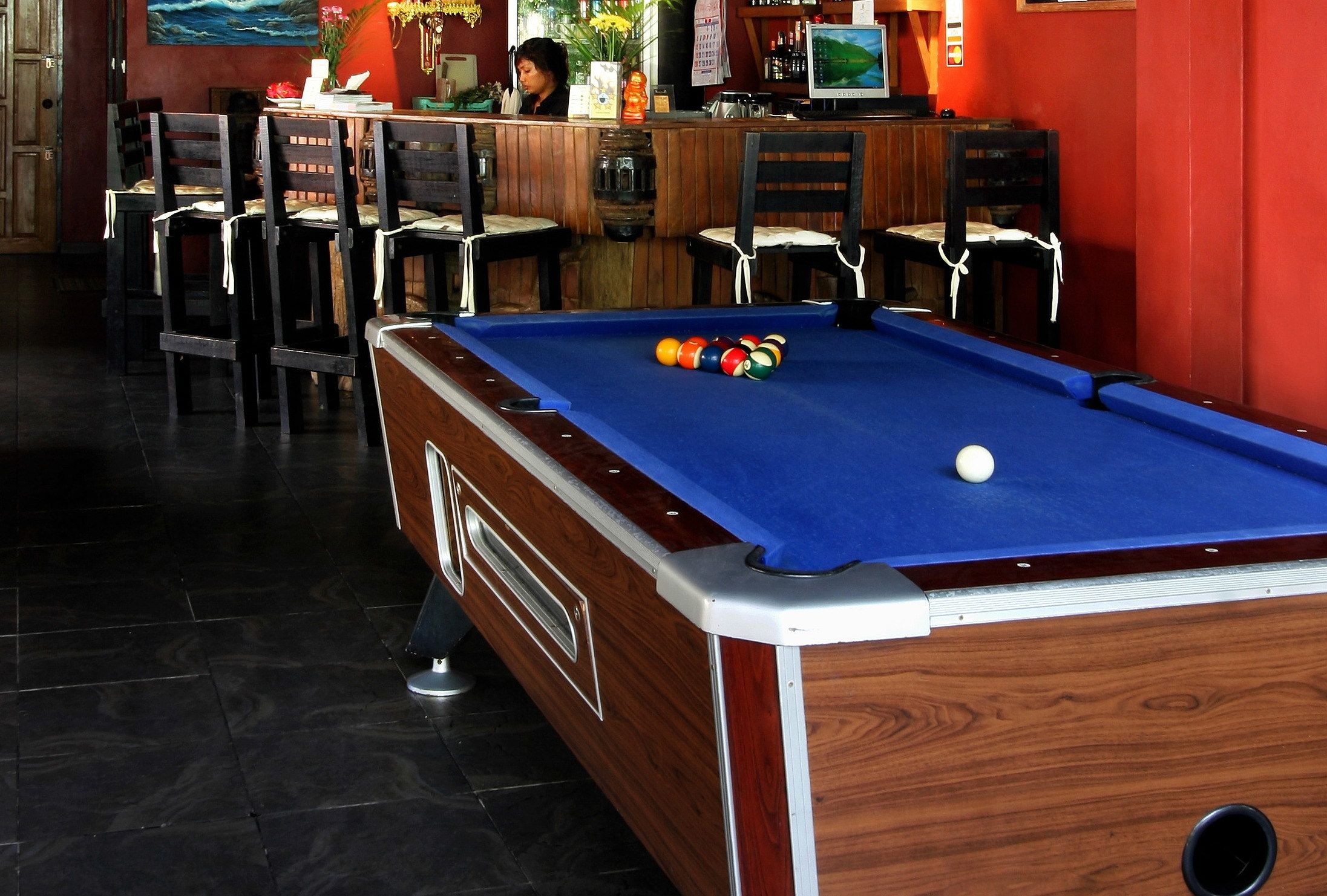 A pool table with balls, a bar area, and several chairs.