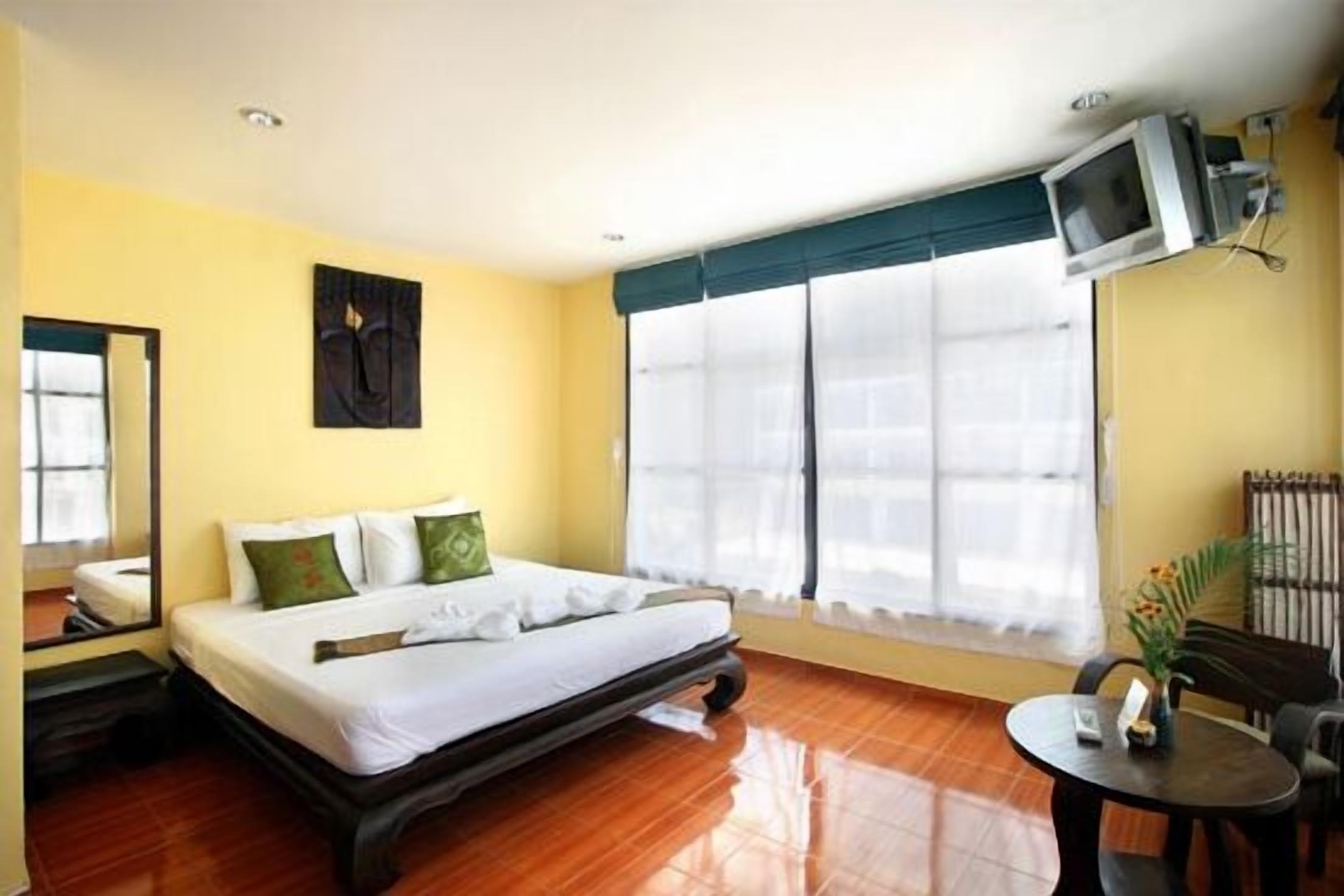 A hotel room with a bed, a small table, a chair, a TV mounted on the wall, and a window with curtains.