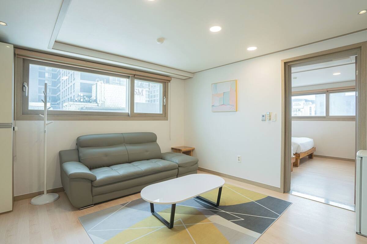 A modern living room with a grey sofa, a small table, and a view of a cityscape through the window.
