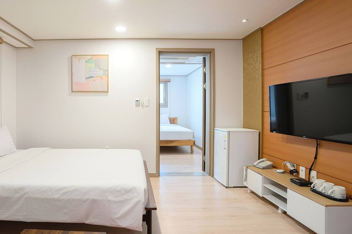 A hotel room with a bed, a TV, a mini-fridge, and a desk with a phone and cups.