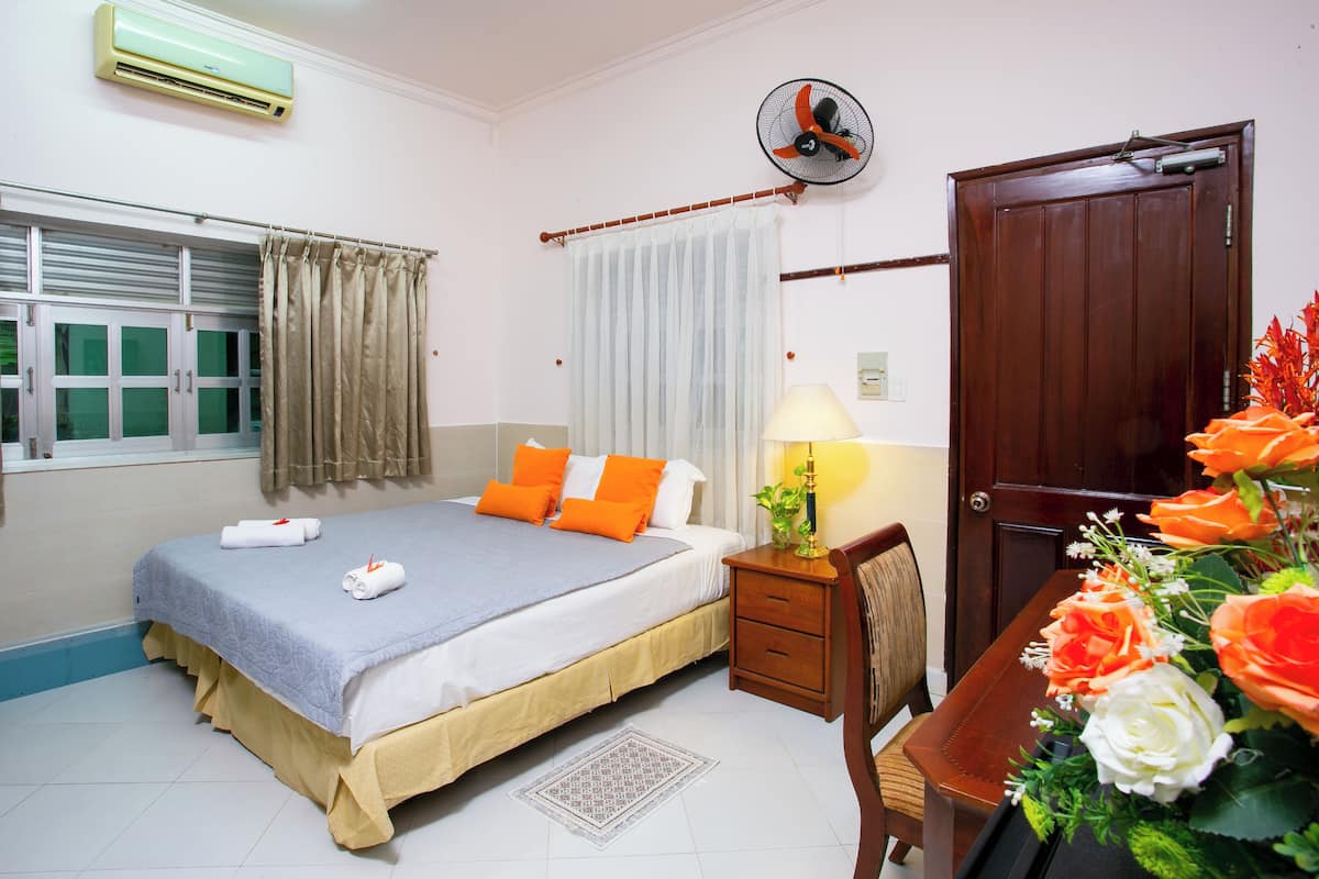 A hotel room with a bed, bedside table, lamp, chair, and a wooden door.