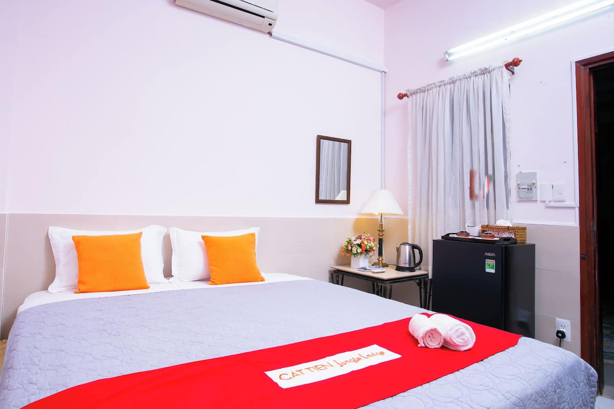 A hotel room with a bed, a desk with a lamp, a refrigerator, and a window with curtains.