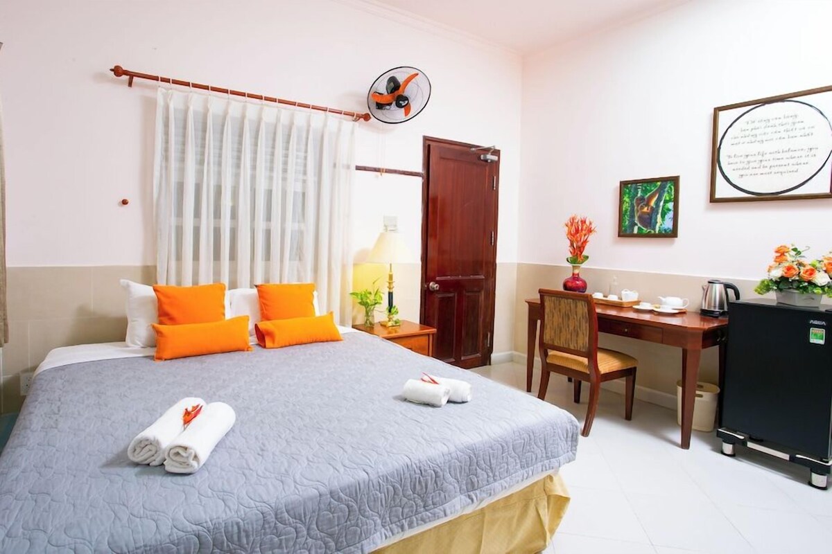 A hotel room with a bed, a desk, a chair, a refrigerator, and a door.
