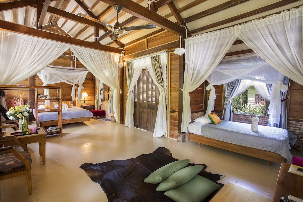 A room with two beds, a wooden ceiling, and a large fur rug.