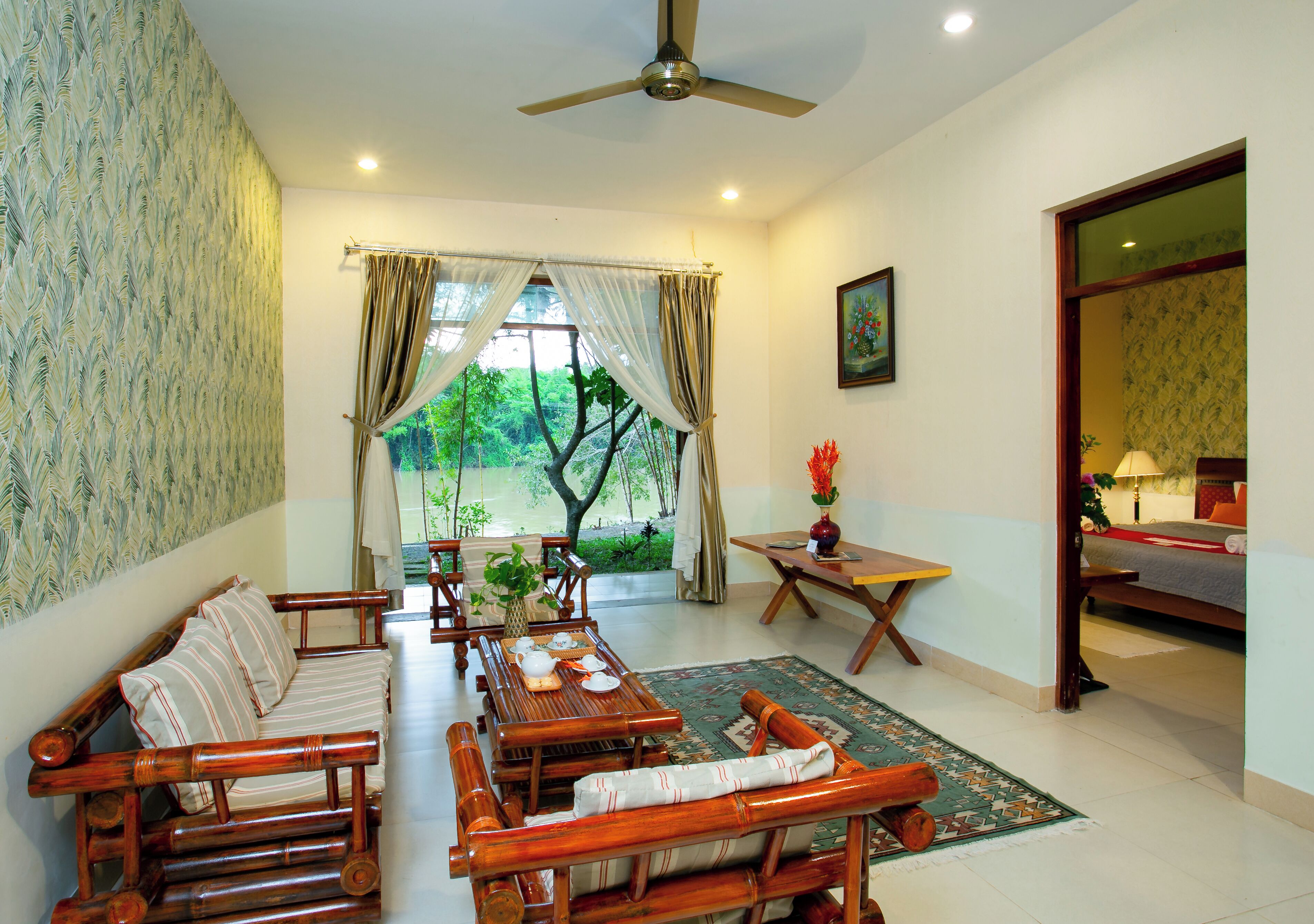 A room with a sofa, dining table, and chairs, a small table with a vase, and a view of greenery outside.