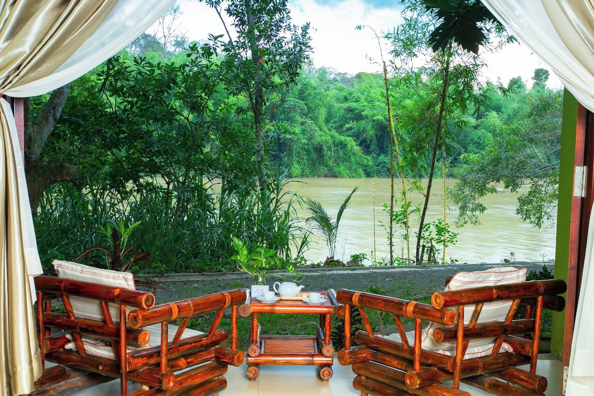 A wooden table with chairs and a view of a river through a window.