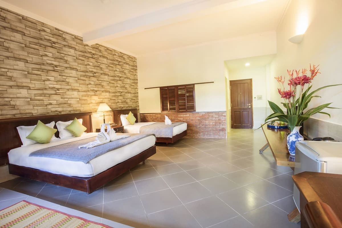 A hotel room with two beds, a stone wall, a wooden door, and a vase with flowers.