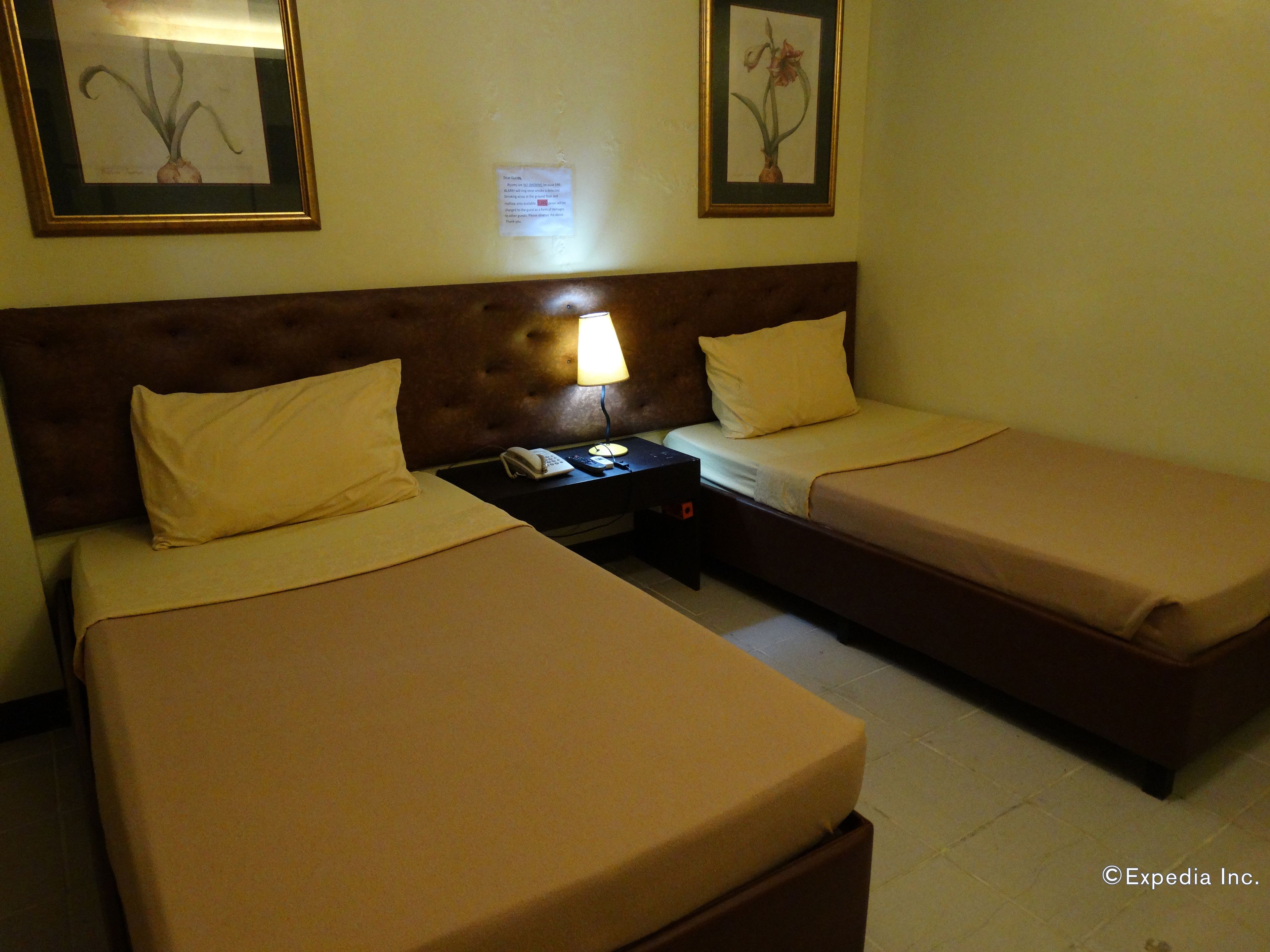 A hotel room with two single beds, a nightstand with a lamp, a phone, and a framed picture on the wall.