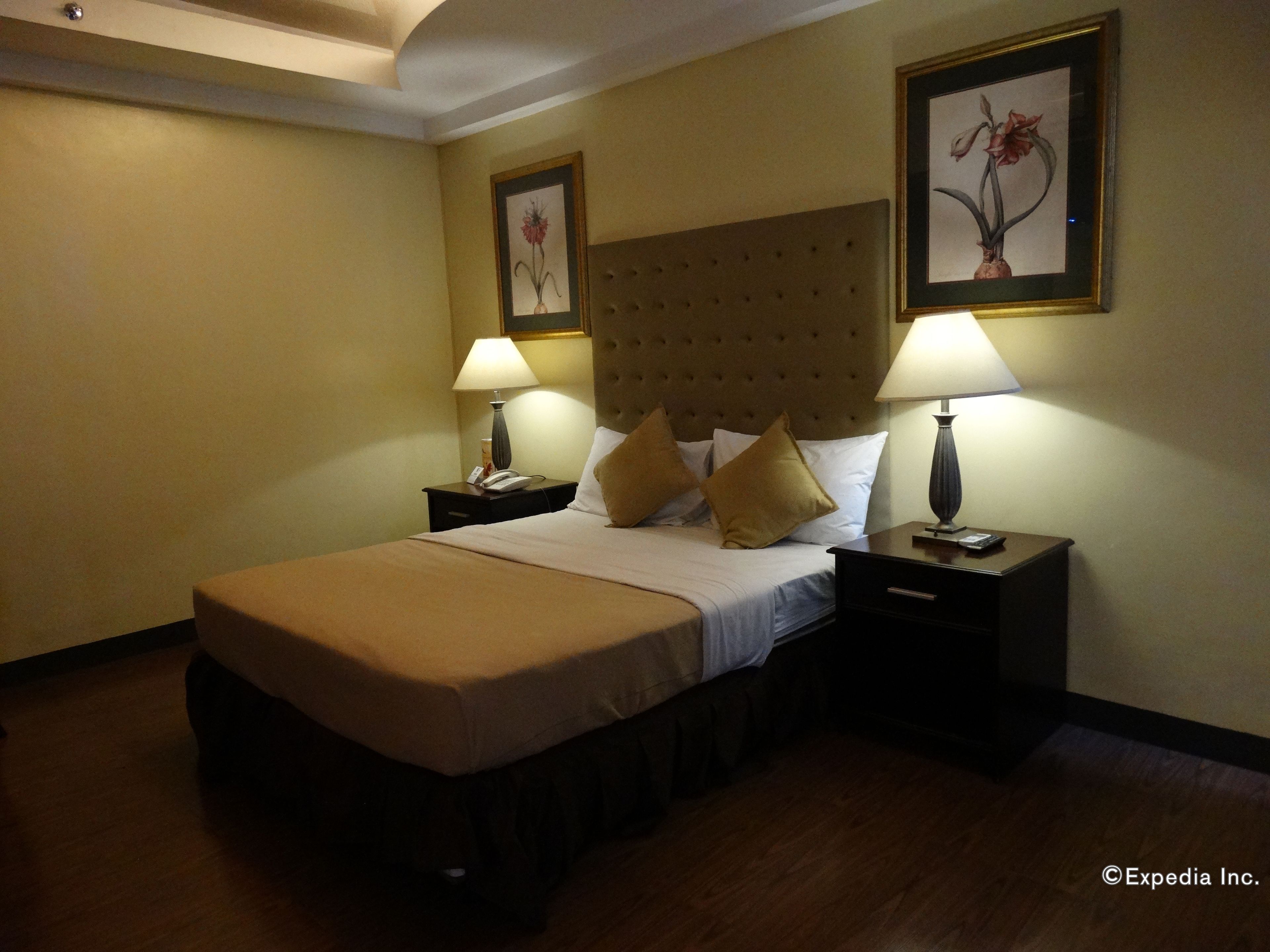 Quarto de hotel com uma cama grande, duas mesas de cabeceira com abajures e duas pinturas florais emolduradas nas paredes.