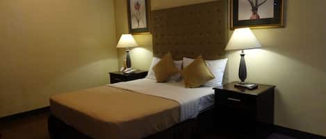A hotel room with a large bed, two bedside tables with lamps, and two framed floral paintings on the walls.