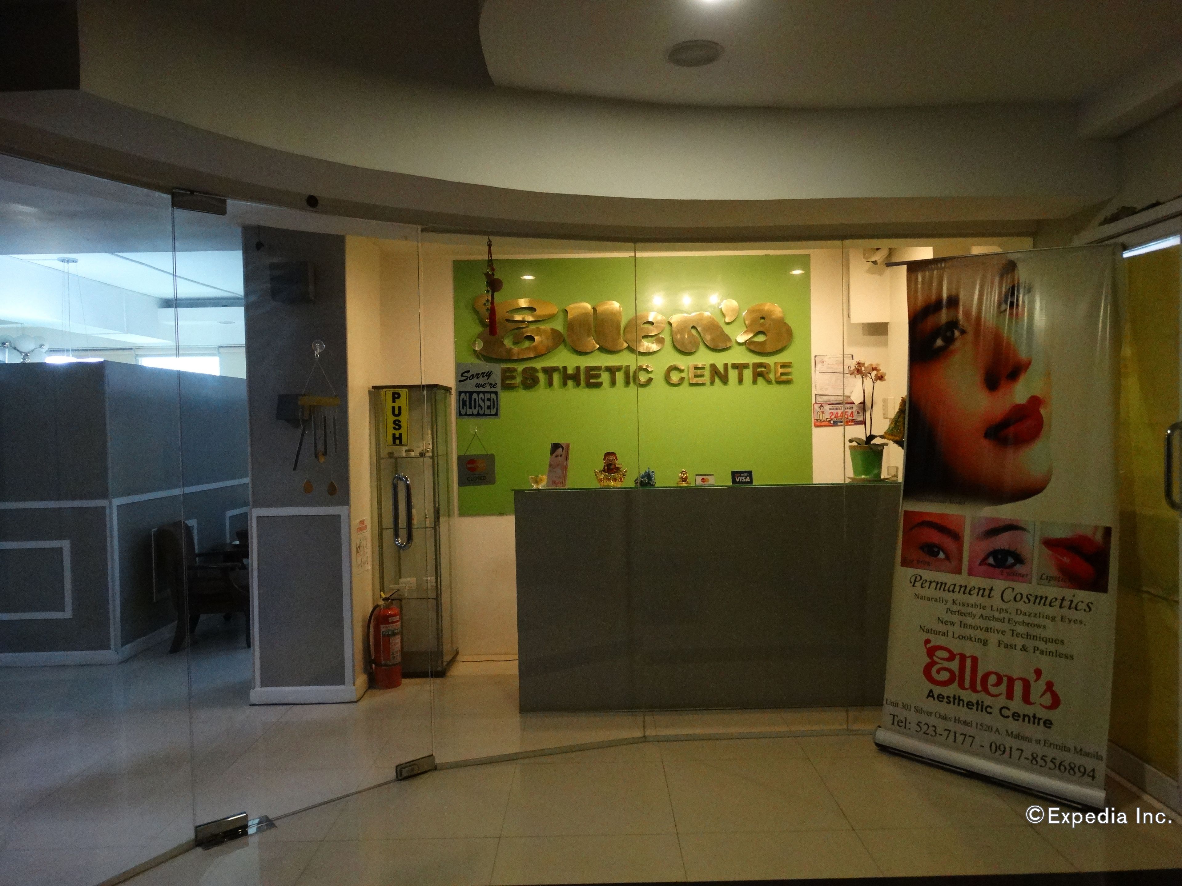 Uma área de recepção com uma parede verde, um balcão de atendimento e um cartaz divulgando serviços de estética.