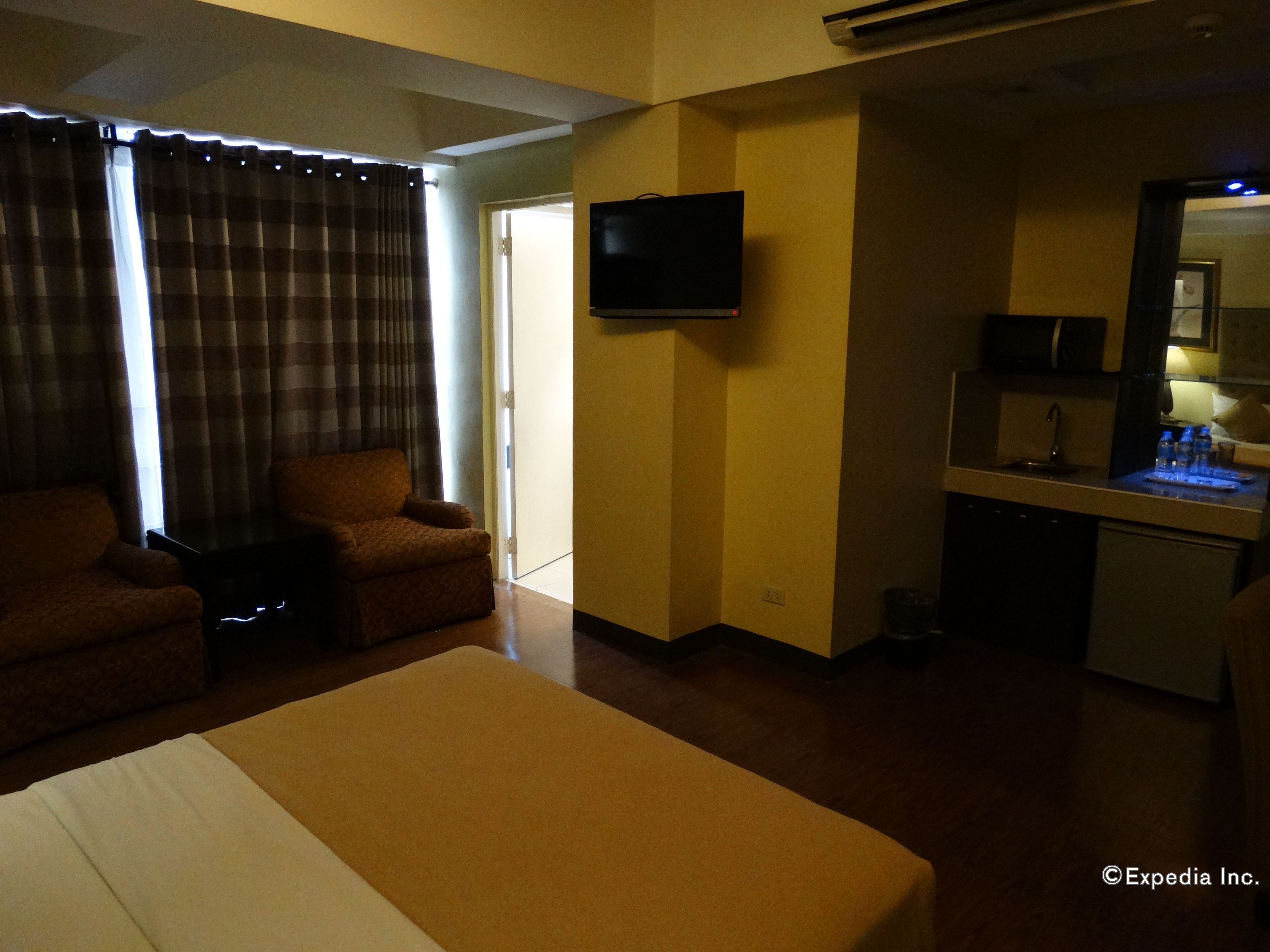 A hotel room with a bed, a sofa, a TV, and a kitchenette.
