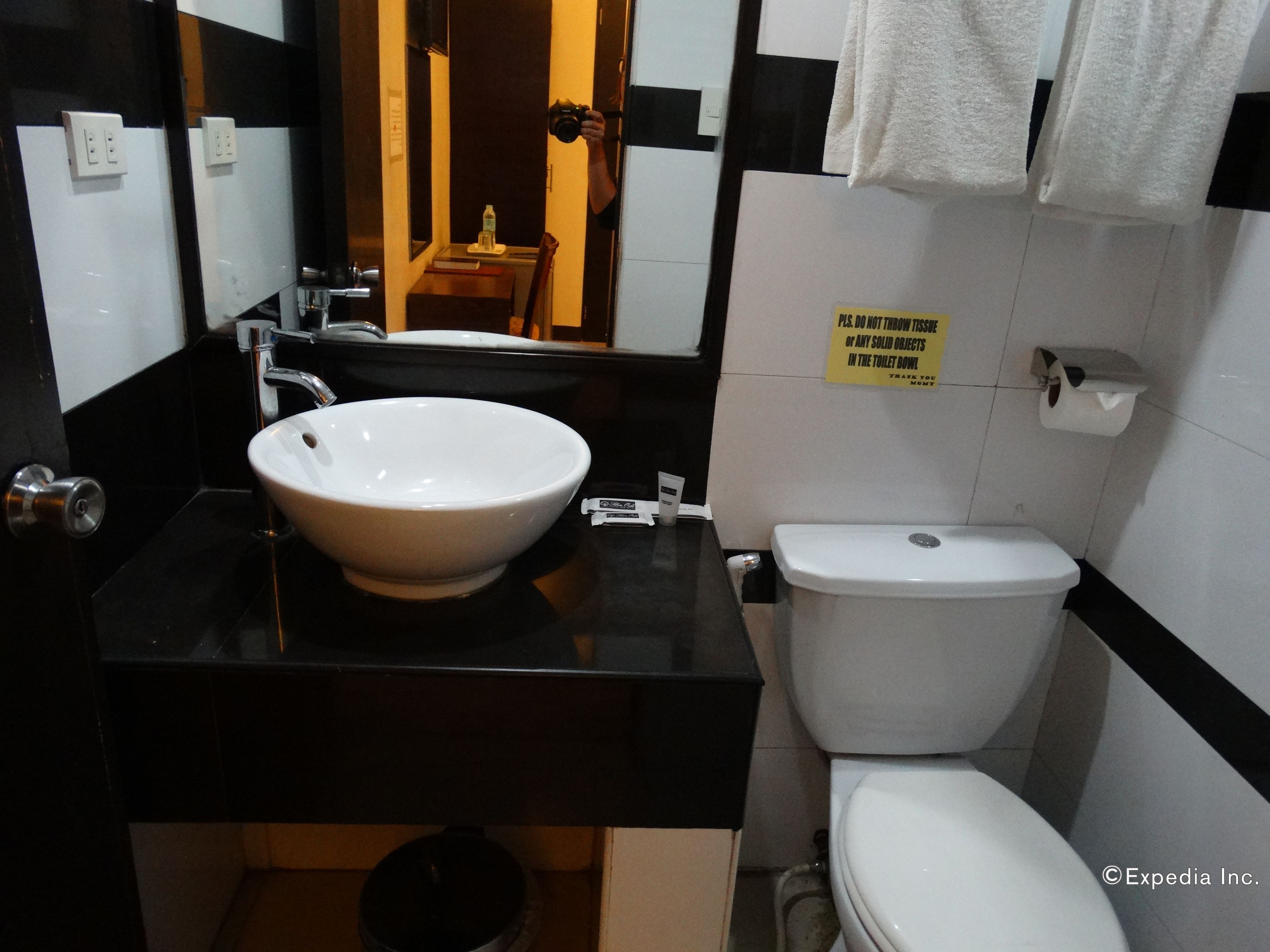 A bathroom with a white sink, black countertop, and a toilet. There is a sign on the wall and a mirror above the sink.