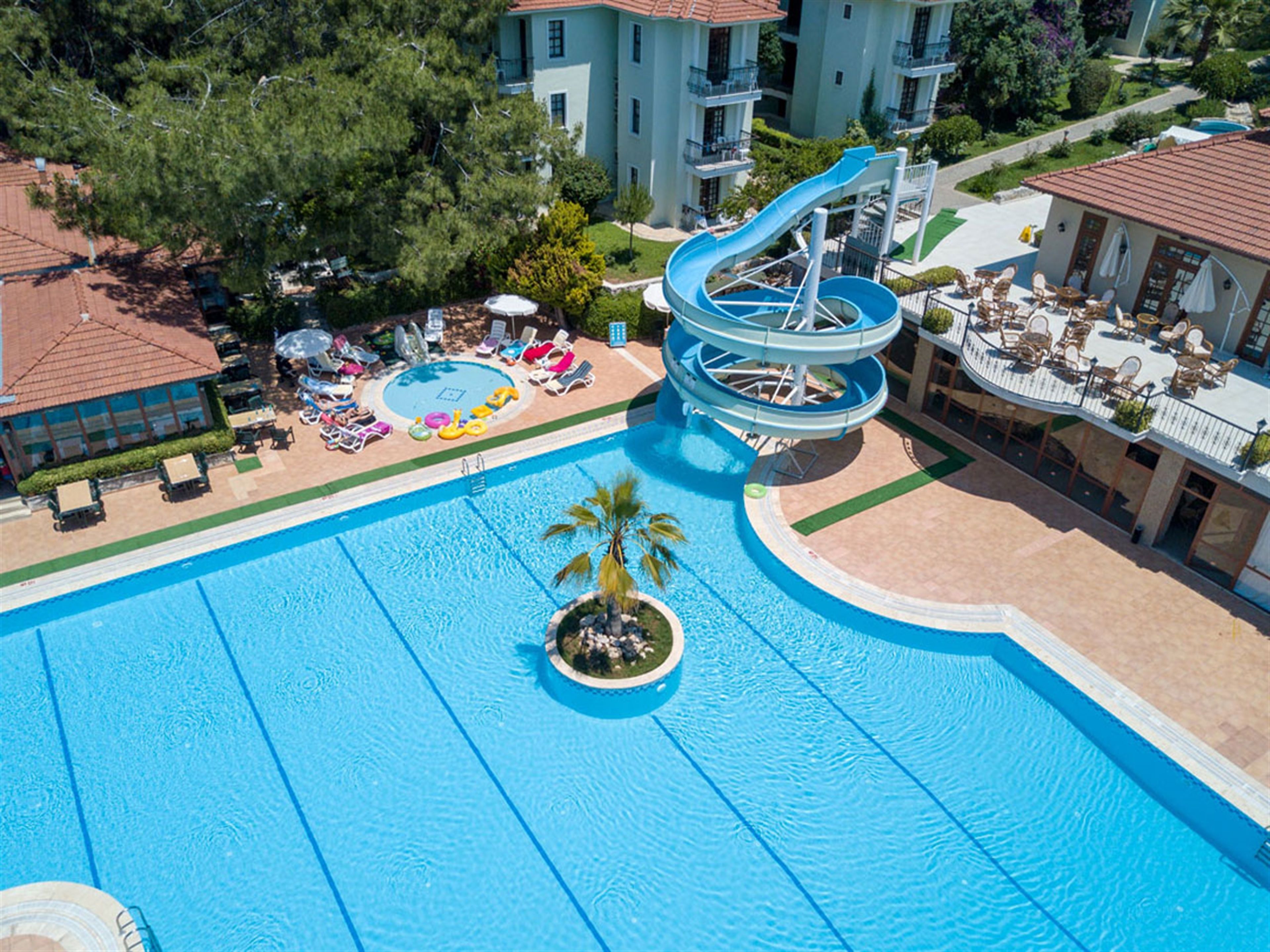 Una gran piscina con tobogán de agua, sillas de descanso y una palmera.