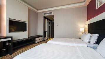 A hotel room with two beds, a TV, a desk, and a door leading to a bathroom.