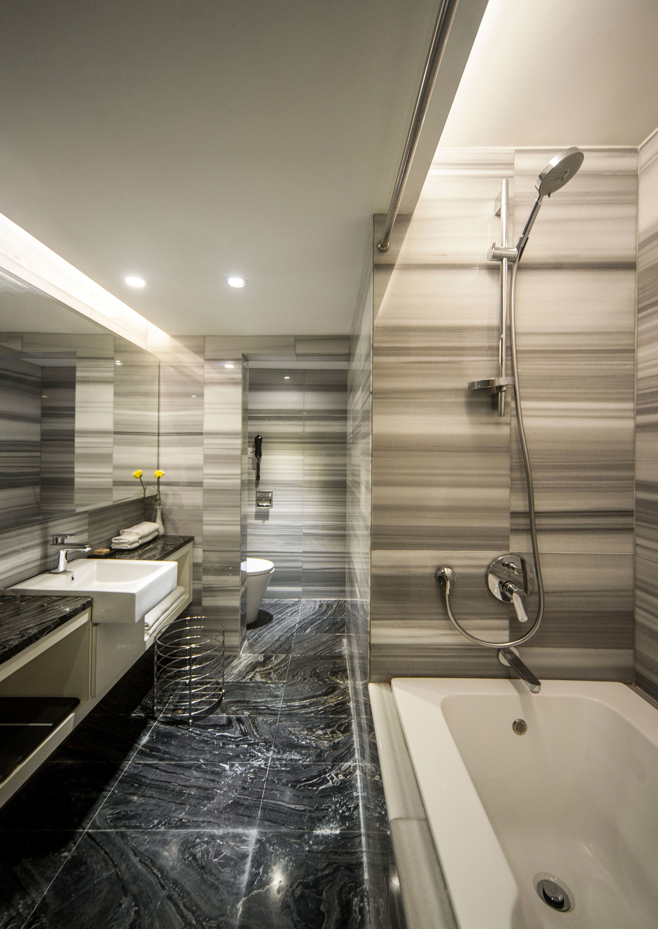 A modern bathroom with a marble floor, a large mirror, a bathtub, and a shower area.