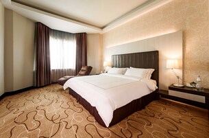 Une chambre d’hôtel avec un grand lit, une chaise, une table de chevet avec une lampe et une moquette à motifs.