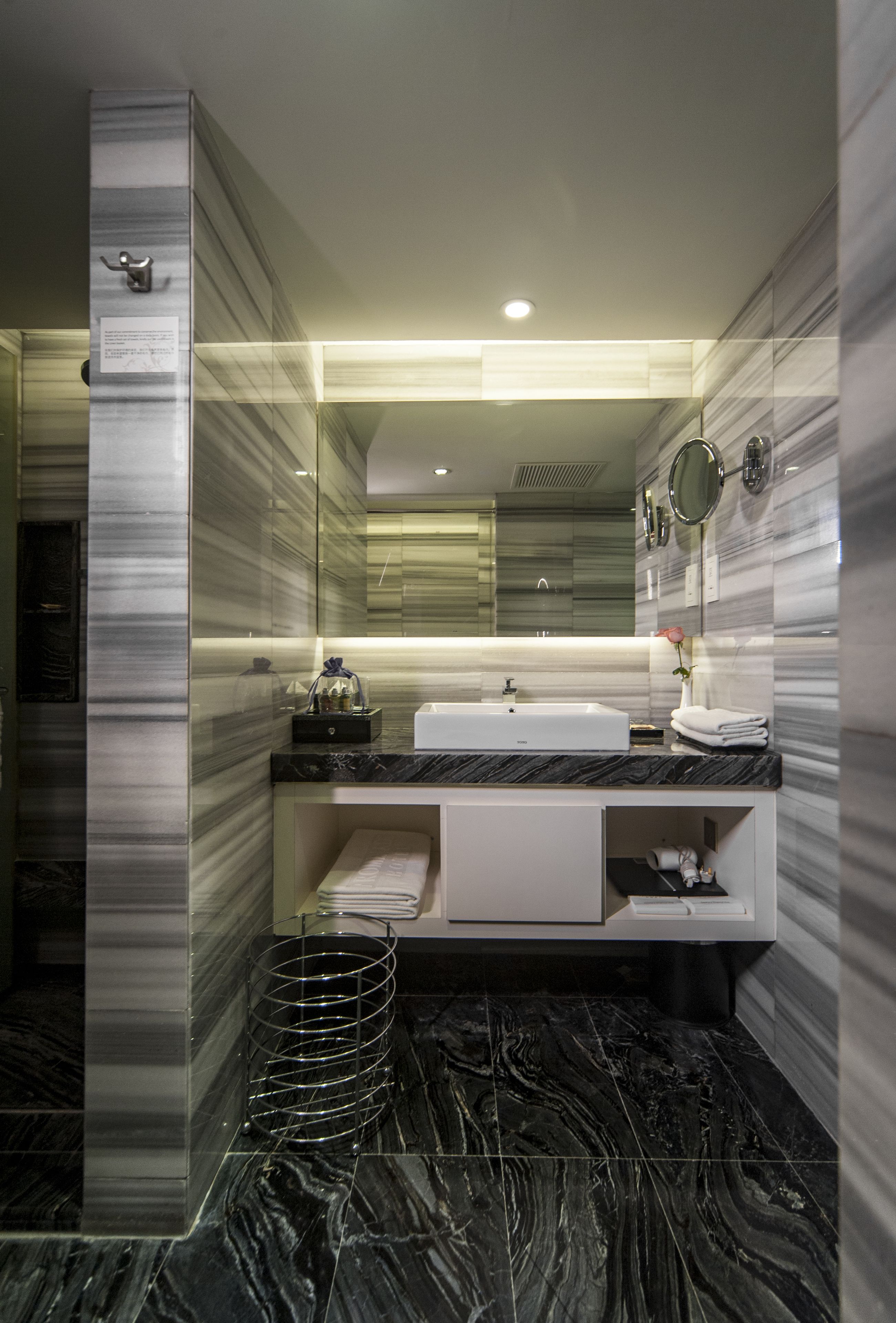 A modern bathroom with a large mirror, a white sink, and a marble floor.