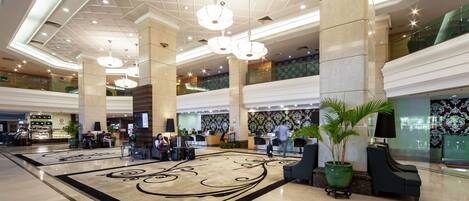 A spacious lobby with high ceilings, large chandeliers, and a central decorative rug.