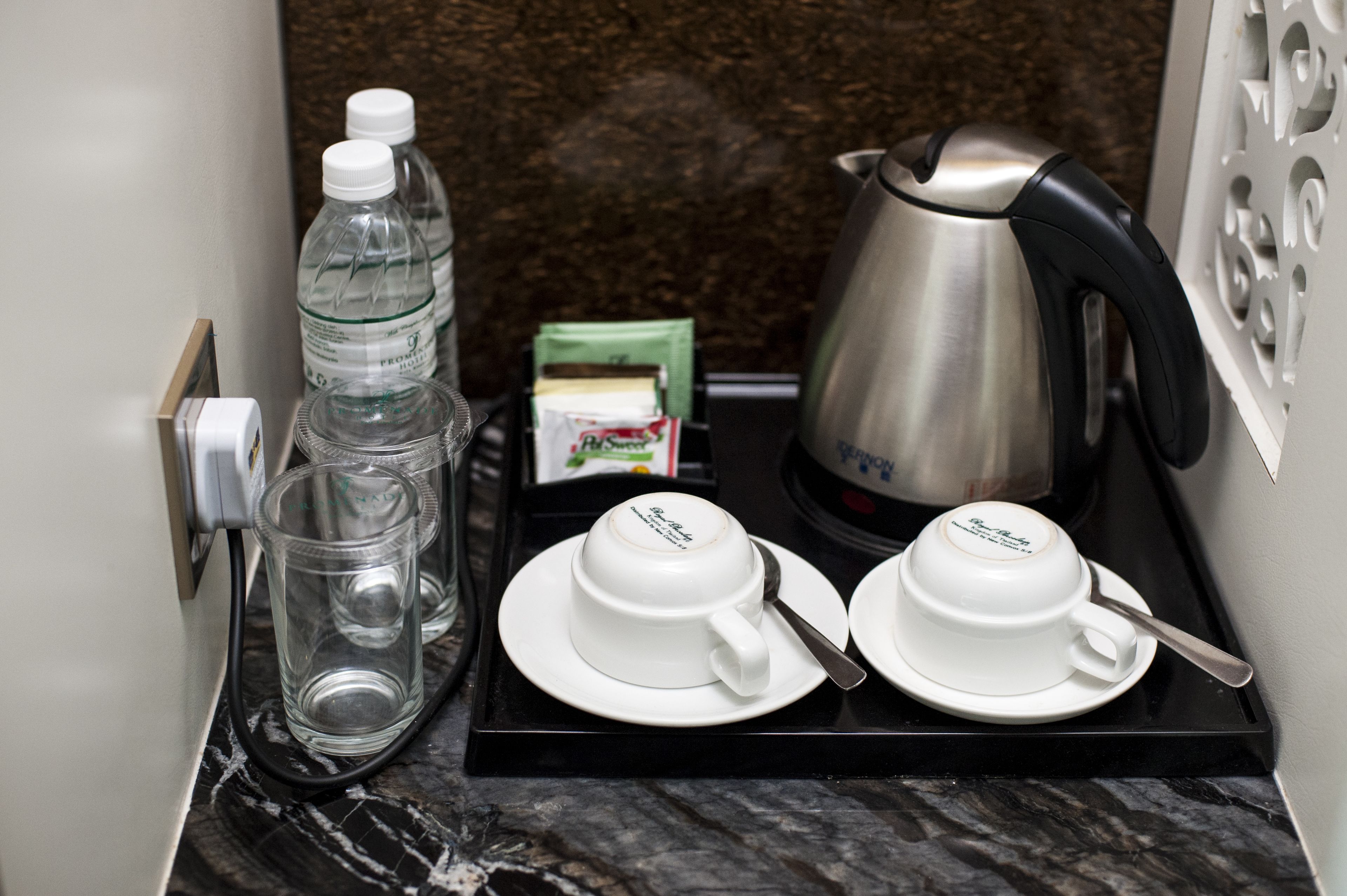 Una bandeja con dos tazas blancas y una tetera eléctrica plateada sobre una encimera de mármol.