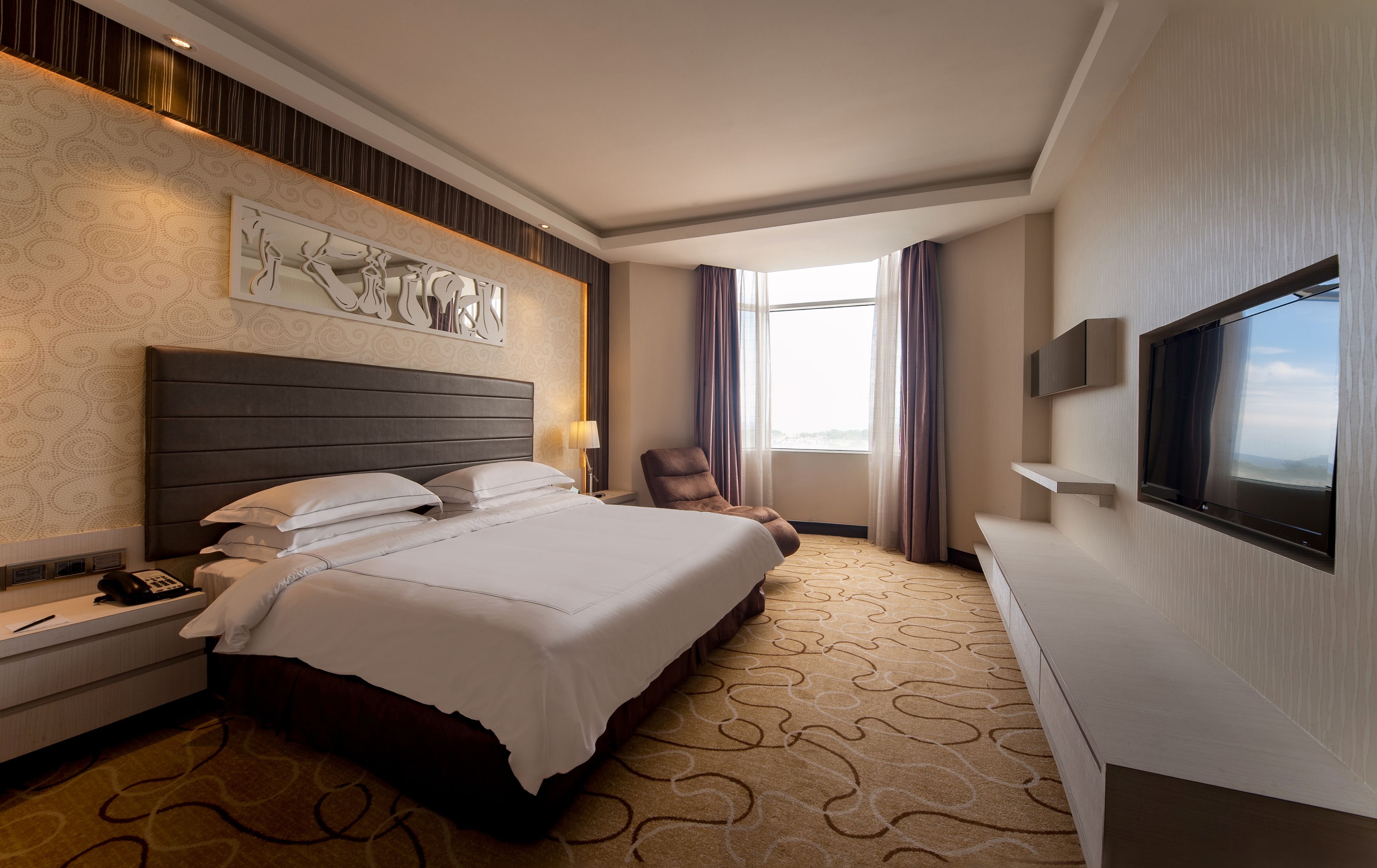 A hotel room with a large bed, a flat-screen TV, a chair, and a desk with a phone.