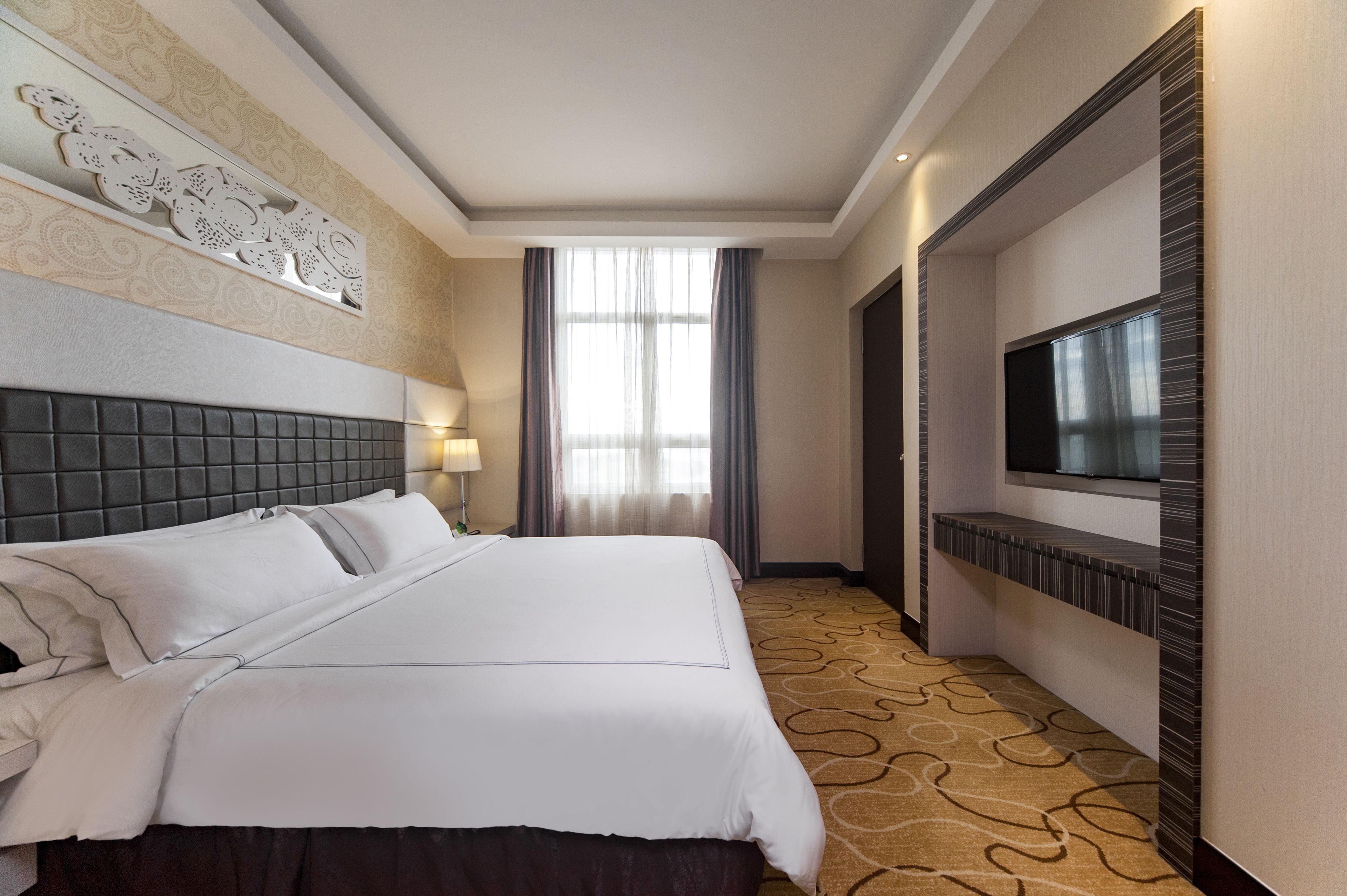 Une chambre d’hôtel avec un grand lit, un téléviseur fixé au mur et un sol recouvert de moquette.