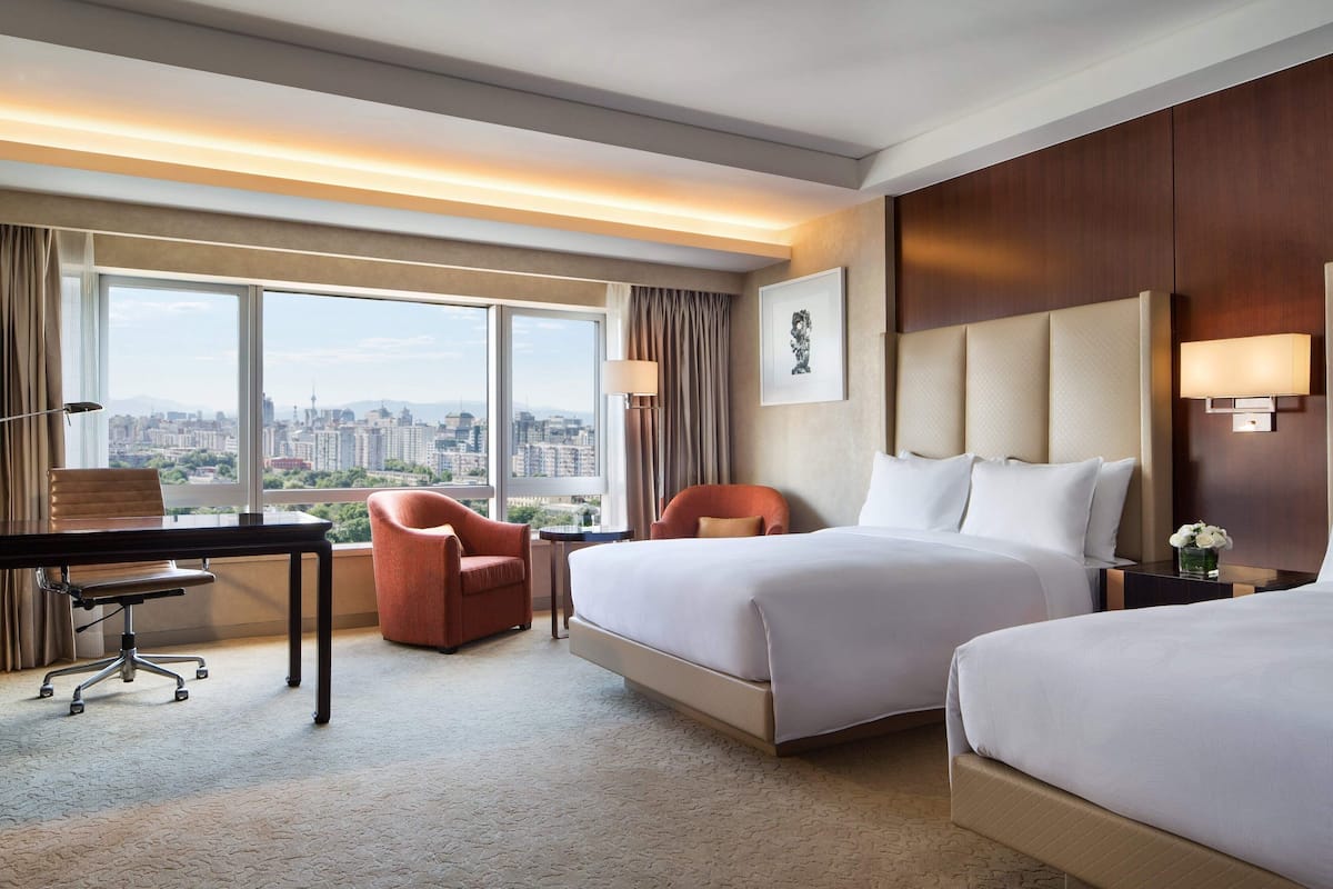 A hotel room with a large bed, a desk, a chair, and a view of the city.