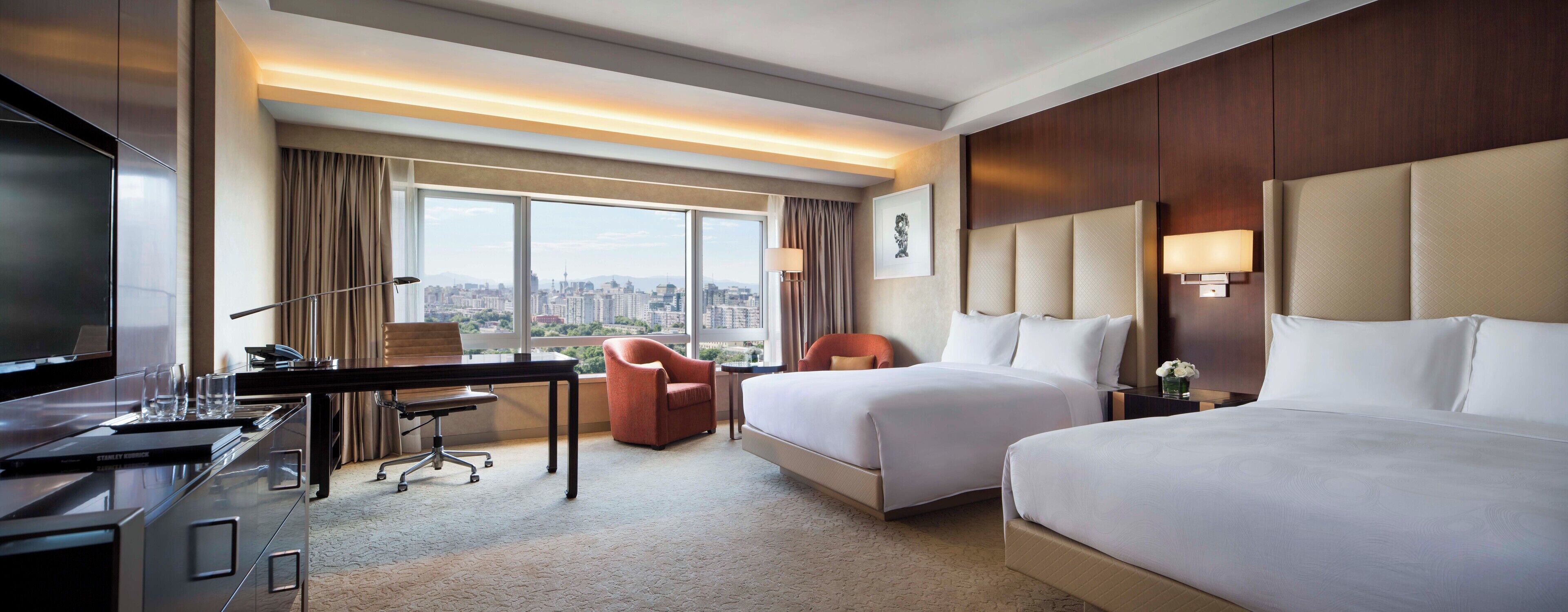 Habitación de hotel con escritorio, dos camas, una silla, televisor y vistas a la ciudad.