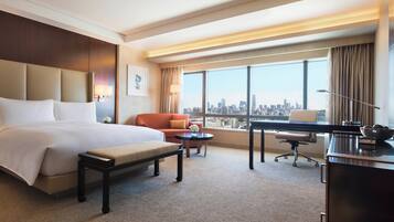 A hotel room with a large bed, a desk, a chair, a small table, and a TV.