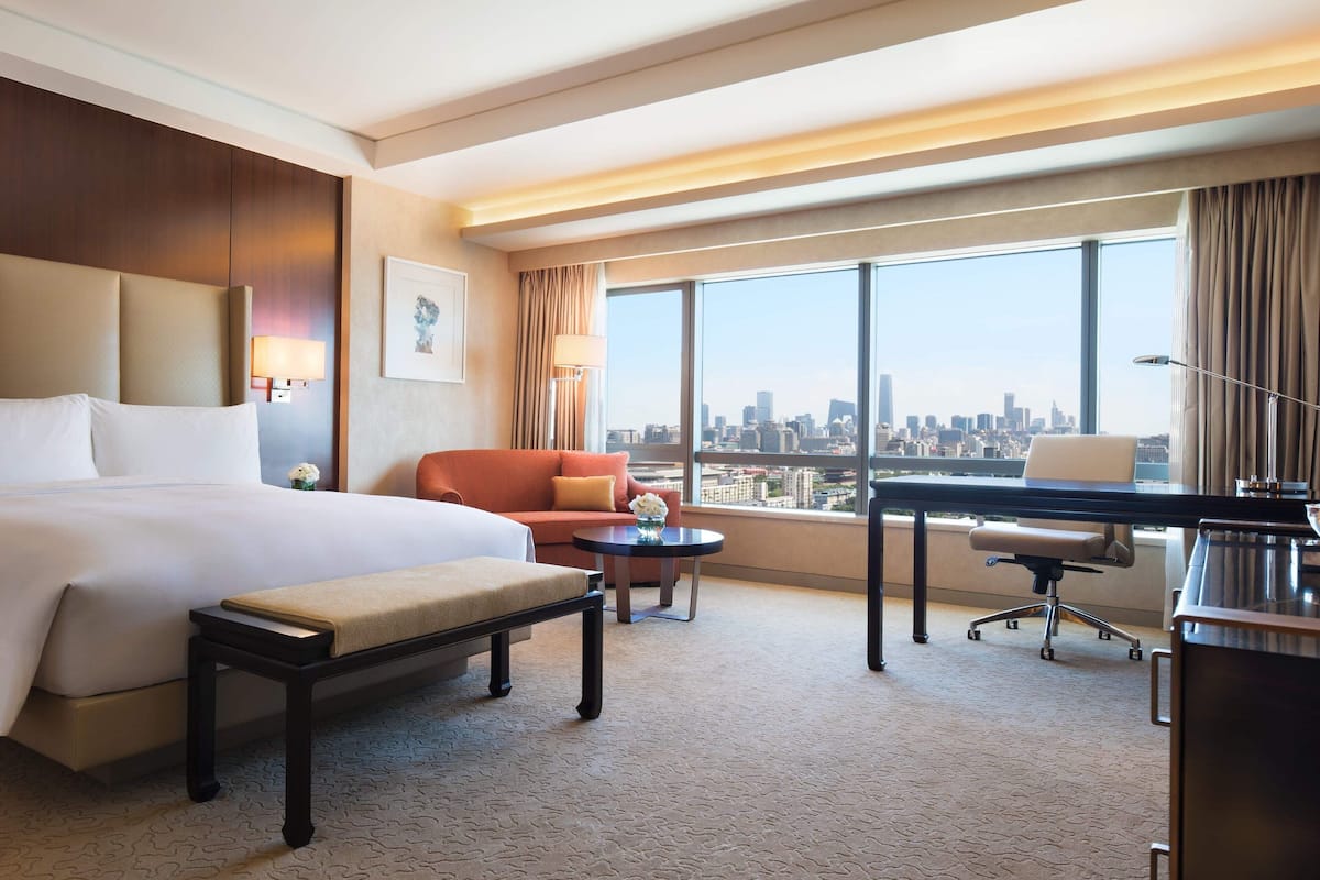 A hotel room with a large bed, a desk, a chair, and a view of the city skyline.