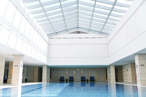 Una piscina interior con techos altos y tragaluces, rodeada de paredes color beige y sillas azules.