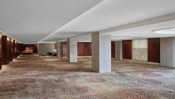 A spacious hotel corridor with a patterned carpet, large columns, and a modern ceiling design.