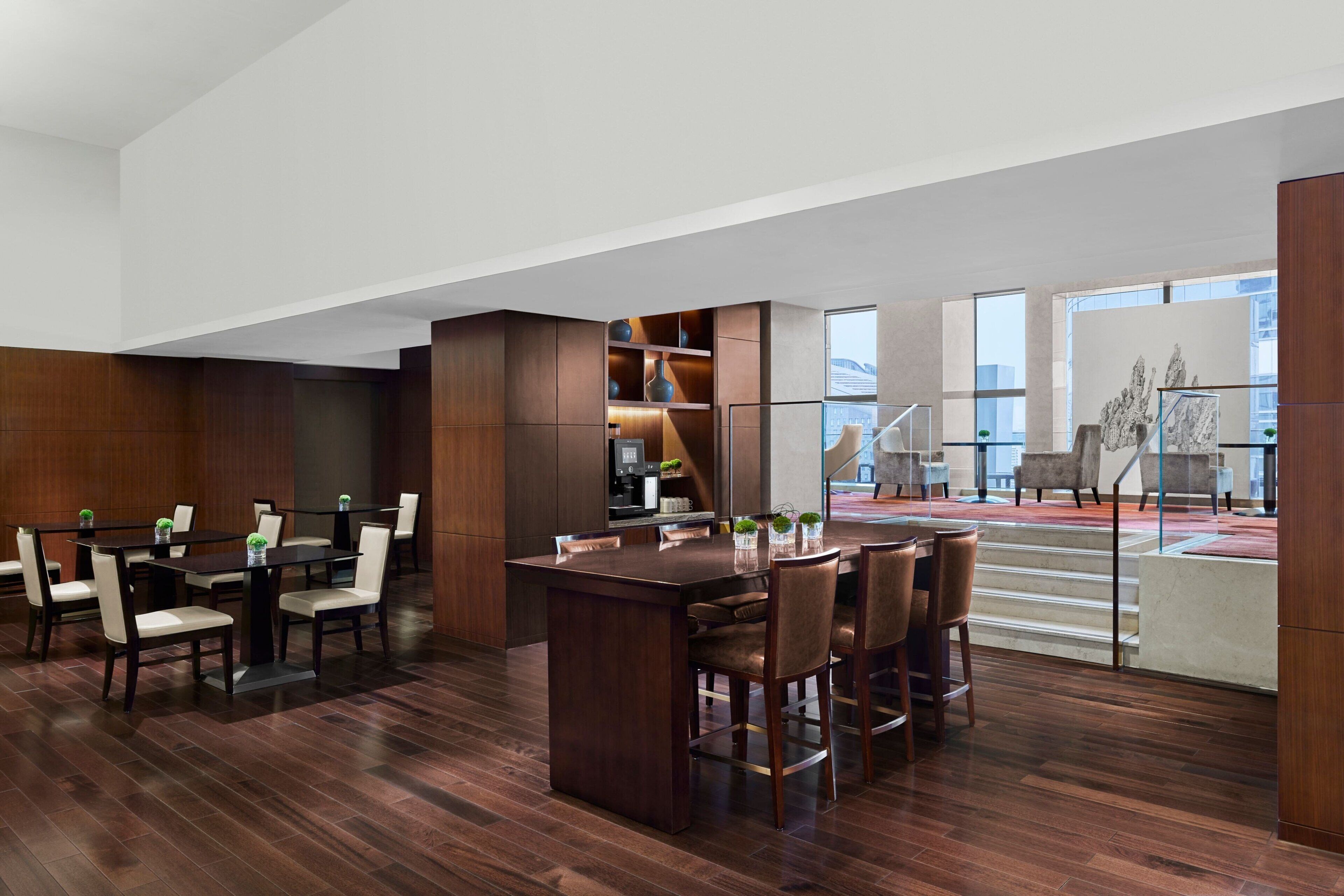A modern hotel lobby with a large wooden reception desk, seating area, and a staircase leading to an upper floor.
