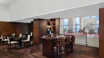 A modern hotel lobby with a large wooden reception desk, seating area, and a staircase leading to an upper floor.