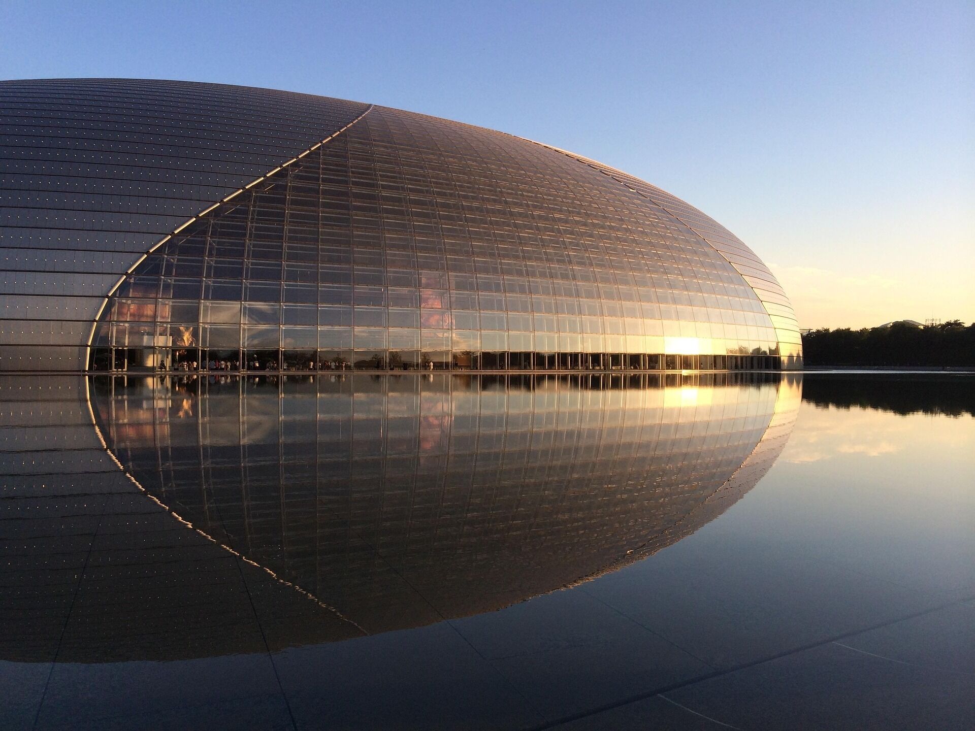 Ein großes, modernes Glasgebäude mit geschwungener Fassade, das sich in ruhigem Wasser spiegelt.