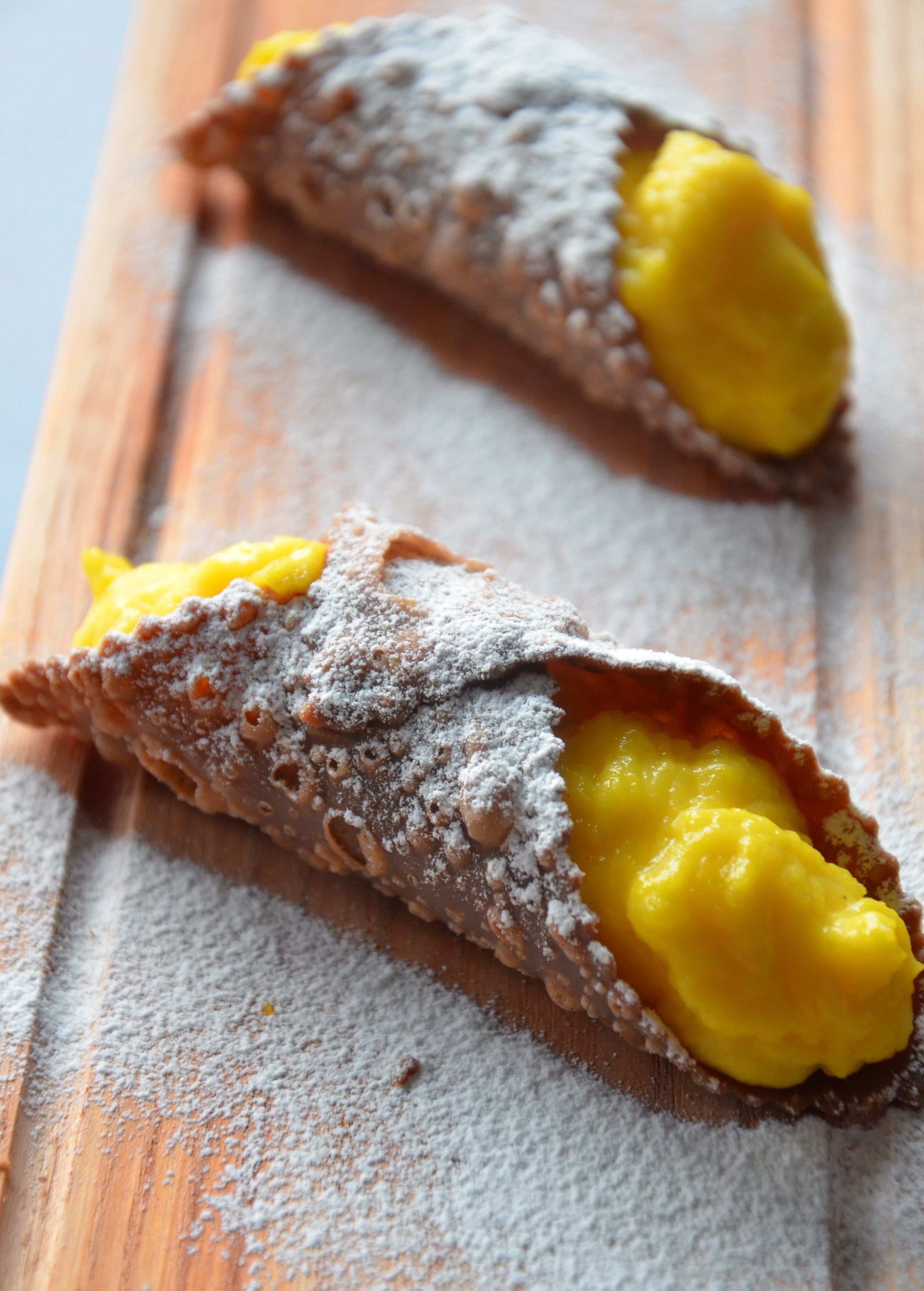 Two cannoli with a dusting of powdered sugar on a wooden surface.