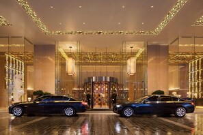 Una entrada de hotel moderna con fachada de vidrio, puerta giratoria y dos coches estacionados frente.