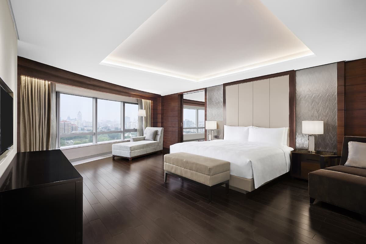 A modern hotel room with a large bed, a sofa, a desk, and a TV.