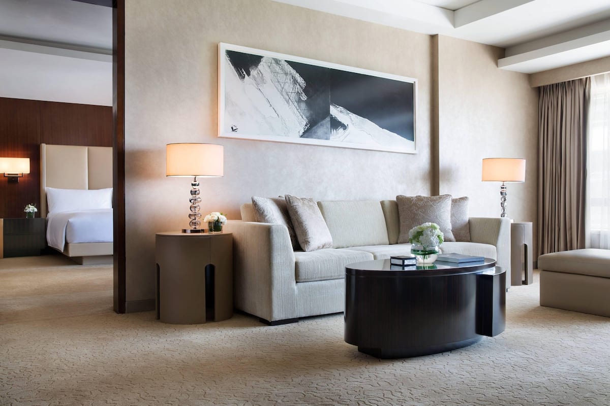 A hotel room with a large bed, a sofa, a coffee table, and a painting on the wall.