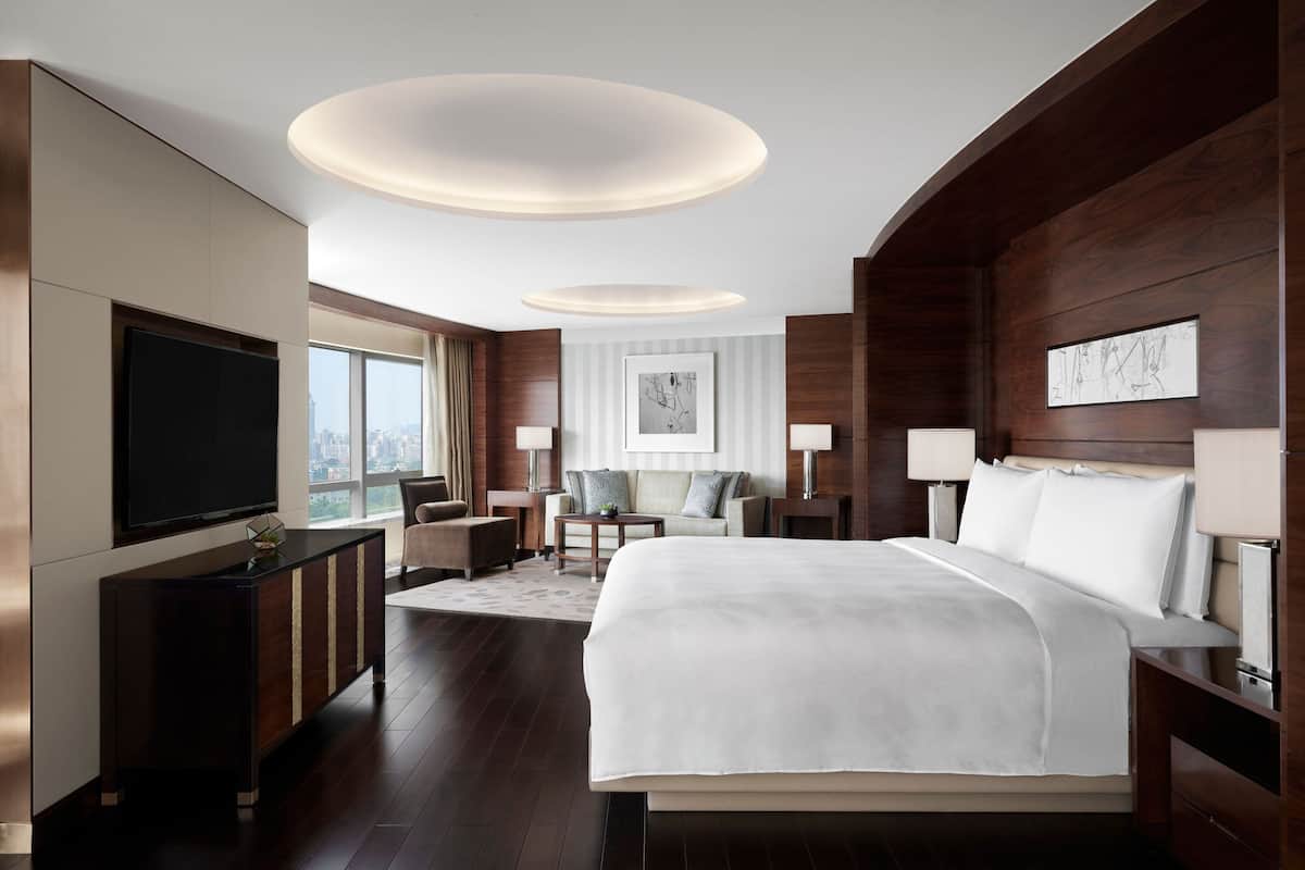 A modern hotel room with a large bed, a flat-screen TV, a desk, and a view of the city.